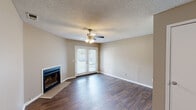 Located at 600 Firestone Ave in Muscle Shoals, Alabama, this single-floor home offers a well-organized layout with a variety of functional living spaces. The main living area is a standout, featuring rich dark hardwood-style flooring, a cozy fireplace with tile surround, and a ceiling fan with light fixture overhead. French doors in the living room provide natural light and outdoor access, complementing the neutral warm-toned walls and textured ceilings found throughout the home. A dedicated entry area with matching hardwood-style flooring and a ceiling fan leads seamlessly into the living space. The galley-style kitchen is appointed with crisp white shaker cabinetry, granite-look countertops, a stainless steel sink, and black appliances, all set above durable hardwood-style flooring. A long hallway with wall sconce lighting connects the living areas to the private bedrooms. The bedrooms feature plush carpet flooring, ceiling fans, and windows with blinds that allow for natural light. The bathroom includes a white vanity with granite-look countertops, ample cabinetry, and tile flooring. Throughout, the home maintains a consistent, clean aesthetic with neutral tones and practical finishes.
