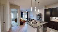 This thoughtfully designed single-floor residence showcases a contemporary aesthetic with clean lines and upscale finishes throughout. The open-concept layout seamlessly connects the kitchen and living area, creating a welcoming and functional shared space. The kitchen is a standout feature, equipped with dark espresso cabinetry that extends to the ceiling, light quartz countertops, a white subway tile backsplash, and a full suite of stainless steel appliances including a refrigerator with ice maker, electric range, and built-in microwave. A kitchen island with an undermount sink and pendant lighting above serves as both a prep area and casual dining space. The living area is warm and inviting, anchored by light wood-look flooring, a ceiling fan, and a large window dressed with navy curtains that allow for ample natural light. The bedroom offers a serene retreat, featuring a bold accent wall, large windows with outdoor views, and access to a generously sized walk-in closet with multi-level shelving and hanging rods. The full bathroom displays refined finishes, including dark cabinetry, a quartz vanity, large-format tile in the shower surround, and a framed mirror. Together, these spaces create a cohesive, modern living environment with thoughtful design details at every turn.