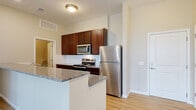 Located at 8891 Moreland St in Powell, Ohio, this single-floor residence offers a well-designed, open-concept layout that blends functionality with modern finishes throughout. The kitchen serves as the centerpiece of the living area, showcasing rich dark wood cabinetry, granite countertops, a white subway tile backsplash, and a full suite of stainless steel appliances including a refrigerator, range, and built-in microwave. A peninsula with additional granite counter space extends into the living area, creating a natural gathering point and enhancing the open flow between the kitchen and main living space. Light-toned hardwood-style flooring runs through the main areas, complementing the neutral, warm wall tones throughout. The bedrooms are carpeted and generously sized, each offering natural light through large windows with exterior views. At least one bedroom features a spacious walk-in closet with wire shelving and hanging rods for ample storage. A dedicated laundry room provides washer and dryer hookups with additional overhead shelving. The bathroom is finished with dark wood vanity cabinetry, granite countertops, and a tub-shower combination. Recessed lighting and flush-mount fixtures illuminate the space, contributing to a clean, bright, and move-in-ready ambiance.