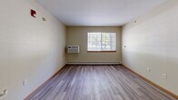 Located at 8800 Macomb St in Grosse Ile, Michigan, this two-bedroom unit offers a well-organized, single-floor layout designed for comfortable everyday living. The combined kitchen and living area serves as the central hub of the unit, featuring light wood-look vinyl flooring, a wall-mounted air conditioning unit, and a bright window that brings in natural light. The kitchen is outfitted with white cabinetry, a full suite of white appliances including a refrigerator, dishwasher, and range, along with ample counter space and a built-in breakfast bar for casual dining. Both bedrooms are carpeted and share a warm, neutral color palette with wood-toned baseboards. Each room includes a window with outdoor views and baseboard heating, ensuring year-round comfort. The primary bedroom is generously sized and connects to a dedicated walk-in closet equipped with wire shelving that spans two walls, offering substantial storage capacity. A second bedroom provides comfortable accommodations for guests or additional occupants. Throughout the unit, the clean, light-toned walls and practical finishes create a functional and welcoming atmosphere suited for a variety of living arrangements.