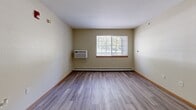 Located at 8800 Macomb St in Grosse Ile, Michigan, this two-bedroom unit offers a well-organized, single-floor layout designed for comfortable everyday living. The combined kitchen and living area serves as the central hub of the unit, featuring light wood-look vinyl flooring, a wall-mounted air conditioning unit, and a bright window that brings in natural light. The kitchen is outfitted with white cabinetry, a full suite of white appliances including a refrigerator, dishwasher, and range, along with ample counter space and a built-in breakfast bar for casual dining. Both bedrooms are carpeted and share a warm, neutral color palette with wood-toned baseboards. Each room includes a window with outdoor views and baseboard heating, ensuring year-round comfort. The primary bedroom is generously sized and connects to a dedicated walk-in closet equipped with wire shelving that spans two walls, offering substantial storage capacity. A second bedroom provides comfortable accommodations for guests or additional occupants. Throughout the unit, the clean, light-toned walls and practical finishes create a functional and welcoming atmosphere suited for a variety of living arrangements.