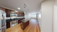Located at 130 Hempstead Ave in West Hempstead, NY, this well-appointed 1-bedroom, 1-bathroom residence offers a thoughtfully designed layout across a single floor. The open-concept living and kitchen area serves as the heart of the home, showcasing rich dark wood cabinetry that reaches to the ceiling, dark granite countertops, and a full suite of stainless steel appliances including a gas range, microwave, refrigerator, and dishwasher. A central kitchen island with a matching granite surface provides additional prep space and a natural gathering point, while sleek pendant lighting adds a modern touch overhead. Warm hardwood flooring flows throughout the main living areas, creating a cohesive and inviting atmosphere. The living room benefits from natural light streaming in through large windows dressed with clean white blinds. The bedroom features soft carpeting underfoot, neutral-toned walls, and a generous window that further brings in natural light. The bathroom is finished with a tiled tub-shower combination, a dark wood vanity with a white countertop, and contemporary wall-mounted lighting. A connecting hallway provides a smooth transition between all rooms, completing this efficient and stylishly finished residence.