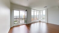 Located in Portland's vibrant Pearl District, this single-floor residence at 1122 NW Glisan St offers a clean, contemporary design with an open and airy feel throughout. Rich hardwood flooring flows seamlessly through the main living areas, complemented by crisp white walls and modern finishes that create a bright, welcoming atmosphere.

The living area is a true highlight, featuring expansive floor-to-ceiling windows on two sides that flood the space with natural light and frame sweeping panoramic views of the Portland skyline. A private balcony is accessible through a full-height glass door, extending the living space outdoors and offering an elevated vantage point over the city.

The kitchen is thoughtfully designed with two-tone cabinetry — warm wood lower cabinets paired with white upper cabinets — along with light countertops, stainless steel appliances including a refrigerator and dishwasher, and a single-basin sink. The bedroom features plush neutral carpeting and clean white walls, providing a calm and restful retreat. The bathroom is finished in white with a full soaking tub and shower combination with chrome fixtures. A long entry hallway connects the spaces efficiently, reinforcing the unit's well-organized layout.