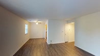This single-floor residence is designed with a practical and straightforward layout that connects key living areas through a central hallway. The entryway opens into a well-lit corridor with recessed lighting and a programmable thermostat, leading into the main living space. The living area is finished with dark wood-look flooring and features a sliding glass door that provides direct access to an outdoor patio while allowing natural light to fill the room. A secondary portion of the living space includes a ceiling fan and connects to the kitchen.

The kitchen is equipped with warm-toned wood cabinetry, dark laminate countertops, a double-basin sink, and black appliances including a dishwasher, over-range microwave, and electric range, alongside a white refrigerator. Wood-look flooring continues throughout this area.

The bedrooms are carpeted and finished in neutral tones. One bedroom features a spacious reach-in closet with a shelving system and bi-fold doors, while another includes a standard closet and a window overlooking outdoor greenery. Both rooms are bright and offer a quiet, comfortable atmosphere.

The bathroom includes a full tub-shower combination with white tile surround, brushed nickel fixtures and accessories, and wood-look flooring. Textured ceilings are consistent throughout the unit.