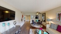 This single-floor residence offers a thoughtfully designed layout that seamlessly connects the main living spaces. The open-concept living and dining area is anchored by rich hardwood-style flooring, a ceiling fan, and a large sliding glass door that floods the room with natural light and provides views of the surrounding greenery. The living area offers generous room for entertaining, while the adjacent dining space comfortably accommodates a round glass table and chairs.

The kitchen is efficiently appointed with dark espresso cabinetry, granite-look countertops, a tiled backsplash, and a full suite of stainless steel appliances including a refrigerator, electric range, and built-in microwave. A pass-through opening connects the kitchen to the main living area, enhancing the open feel of the home.

The bedroom is a calm retreat featuring a distinctive accent wall, hardwood-style flooring, a natural window for light, and direct access to a vanity area. The bathroom includes a full soaking tub with shower, white tile surround, a frosted window, and clean, bright finishes throughout.

A smart home thermostat and textured ceilings are consistent throughout the unit, adding functional and architectural character to this well-balanced residential space.