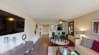 This single-floor residence offers a thoughtfully designed layout that seamlessly connects the main living spaces. The open-concept living and dining area is anchored by rich hardwood-style flooring, a ceiling fan, and a large sliding glass door that floods the room with natural light and provides views of the surrounding greenery. The living area offers generous room for entertaining, while the adjacent dining space comfortably accommodates a round glass table and chairs.

The kitchen is efficiently appointed with dark espresso cabinetry, granite-look countertops, a tiled backsplash, and a full suite of stainless steel appliances including a refrigerator, electric range, and built-in microwave. A pass-through opening connects the kitchen to the main living area, enhancing the open feel of the home.

The bedroom is a calm retreat featuring a distinctive accent wall, hardwood-style flooring, a natural window for light, and direct access to a vanity area. The bathroom includes a full soaking tub with shower, white tile surround, a frosted window, and clean, bright finishes throughout.

A smart home thermostat and textured ceilings are consistent throughout the unit, adding functional and architectural character to this well-balanced residential space.
