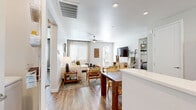 This thoughtfully designed single-story home offers four bedrooms and three bathrooms across a comfortable, efficiently planned floor plate. The open-concept living and dining area serves as the heart of the home, featuring wood-look flooring, a ceiling fan, and abundant natural light streaming through multiple windows and a glass exterior door. The space flows seamlessly into the kitchen, which is outfitted with white shaker cabinetry, stainless steel appliances, a breakfast bar with counter seating, and clean white countertops — ideal for both everyday living and entertaining. The living room provides a welcoming retreat with a large sectional sofa, curated gallery wall, and warm, neutral tones throughout. The primary bedroom is a spacious haven with natural light, wood-look flooring, and access to a dedicated walk-in closet featuring multi-level hanging rods and built-in shelving. Additional bedrooms maintain the home's consistent aesthetic with soft tones, natural light, and wood-look flooring. The bathrooms are finished with light cabinetry, white countertops, and tub-shower combinations. Two hallways connect the layout efficiently. The home's cohesive palette of whites, grays, and warm wood tones creates a modern yet inviting ambiance throughout every room.
