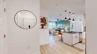 This single-floor, 3-bedroom, 2-bathroom residence combines modern design with practical functionality across a well-organized open-concept layout. The welcoming entrance, accented by a circular wall mirror and curated artwork, leads directly into the combined kitchen and living area. The kitchen is a standout feature, outfitted with crisp white shaker cabinetry, dark granite countertops, a classic subway tile backsplash, stainless steel appliances, and light hardwood-style flooring that flows throughout the main living areas. The open living room is bright and airy, benefiting from large windows that invite natural light, and is anchored by a ceiling fan overhead and a bold teal accent wall that adds a vibrant focal point. The three bedrooms are carpeted for comfort, each featuring windows with outdoor views and ceiling fans. The primary bedroom includes a dedicated walk-in closet with built-in wire shelving for ample storage. Both bathrooms are finished with white cabinetry, dark countertops, and hardwood-style flooring; one features a tub-shower combination with white tile surround, while the other offers a long vanity with built-in shelving. The overall ambiance is clean, contemporary, and inviting.