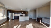 This contemporary two-story residence showcases a thoughtfully designed open-concept layout that blends modern aesthetics with functional living. The kitchen serves as the centerpiece of the main level, featuring rich dark espresso cabinetry extending to the ceiling, granite countertops, a white subway tile backsplash, and a full suite of stainless steel appliances including a refrigerator, electric range, and microwave. A large central island with a built-in sink and matching granite surface provides additional workspace and seating, while pendant lighting adds a refined touch overhead. Wood-look flooring flows throughout the main living areas, enhancing the warm, contemporary feel. Natural light pours in through generously sized windows, brightening each room. The bedrooms are carpeted for comfort and include ceiling fans, with one bedroom offering an outdoor view through a large picture window. A walk-in closet with built-in rod shelving provides ample storage. The bathrooms are finished with the same dark cabinetry and granite countertops found in the kitchen, maintaining a cohesive design language throughout. One bathroom features a glass-enclosed walk-in shower and wood-look tile flooring, while another includes a dual-sink vanity with a large mirror. A central staircase connects both floors, completing this well-appointed home.