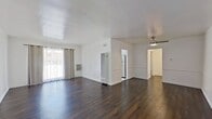 Located at 1737 N Orange Dr, Unit 28 in Hollywood, CA, this 710-square-foot, one-bedroom, one-bathroom apartment delivers a clean and functional layout across a single floor. The combined living room and kitchen area forms the heart of the unit. The living room features rich, dark hardwood floors, crisp white walls, and a large window with grommet-panel curtains that invite natural light. A wall-mounted AC unit provides climate control throughout the space. The galley-style kitchen is outfitted with ample white cabinetry extending to the ceiling, white countertops, classic hexagonal tile flooring, and a full-size stainless steel refrigerator. The 180-square-foot primary bedroom continues the dark hardwood flooring and is equipped with a ceiling fan with light fixture, a window with blinds, and a wall-mounted AC unit. A standout feature of the bedroom is the expansive built-in white closet system with sliding panel doors and overhead cabinetry, maximizing storage. The bathroom is finished with hexagonal mosaic tile flooring, a white soaking tub, a wood-toned vanity with gold hardware, and a window for natural ventilation. A hallway connects the main living areas, completing this well-appointed Hollywood apartment.