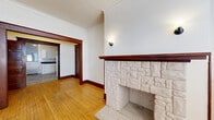 This 2-bedroom, 1-bathroom residence showcases a blend of classic architectural character and functional design across a single floor. The living room serves as the centerpiece of the home, highlighted by a striking white stone fireplace with a rich wood mantel, warm hardwood floors, crown molding, and large dark-trimmed windows that invite natural light. A wall sconce adds a touch of ambient warmth to the space. The layout includes two living areas, offering flexibility for a dedicated sitting or dining space, each connected by well-defined hallways featuring elegant dark wood door frames and trim that carry a consistent traditional aesthetic throughout. The kitchen is equipped with white shaker-style cabinetry, dark countertops, and marble-look tile flooring, offering a clean and functional workspace. The bedrooms are comfortably sized with hardwood floors, natural light from windows, and classic panel-style wood doors. The bathroom is neatly finished with white subway tile, a vessel sink atop a vanity with hex tile detailing, a soaking tub, and a frosted window. An entry closet provides convenient storage near the front door. Radiator heating is present throughout, further reflecting the home's timeless character.
