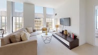 Located at 777-799 Main Street in downtown Hartford, Connecticut, this well-appointed single-floor residence combines contemporary design with functional living. The open-concept living and dining area serves as the heart of the home, anchored by dramatic floor-to-ceiling windows that flood the space with natural light and frame striking panoramic views of the Hartford skyline and surrounding cityscape. The living room features neutral carpeting, a modern media console, and a geometric coffee table, creating an inviting and stylish atmosphere. The kitchen is outfitted with rich wood-grain cabinetry, light quartz countertops, stainless steel appliances, and large-format tile flooring, offering both practicality and modern aesthetic appeal. The primary bedroom is generously sized, benefiting from the same expansive windows and sweeping outdoor views, with soft carpeting and ample room for furnishings. A secondary bedroom provides a quieter, cozier retreat with clean white walls and plush carpeting. The bathroom is finished with slate-toned tile flooring, a floating wood vanity, dual mirrors, and a shower-tub combination. An in-unit laundry area adds everyday convenience. Throughout, the residence maintains a cohesive, light-filled palette that emphasizes clean lines and modern urban living.