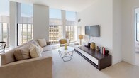 Located at 777-799 Main Street in downtown Hartford, Connecticut, this well-appointed single-floor residence combines contemporary design with functional living. The open-concept living and dining area serves as the heart of the home, anchored by dramatic floor-to-ceiling windows that flood the space with natural light and frame striking panoramic views of the Hartford skyline and surrounding cityscape. The living room features neutral carpeting, a modern media console, and a geometric coffee table, creating an inviting and stylish atmosphere. The kitchen is outfitted with rich wood-grain cabinetry, light quartz countertops, stainless steel appliances, and large-format tile flooring, offering both practicality and modern aesthetic appeal. The primary bedroom is generously sized, benefiting from the same expansive windows and sweeping outdoor views, with soft carpeting and ample room for furnishings. A secondary bedroom provides a quieter, cozier retreat with clean white walls and plush carpeting. The bathroom is finished with slate-toned tile flooring, a floating wood vanity, dual mirrors, and a shower-tub combination. An in-unit laundry area adds everyday convenience. Throughout, the residence maintains a cohesive, light-filled palette that emphasizes clean lines and modern urban living.
