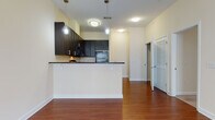 Located at 3050 Milltowne Drive in Ellicott City, Maryland, this two-floor residence offers a well-appointed layout designed for comfortable living. The main level features rich hardwood flooring that flows throughout an open-concept living and dining area, creating a warm and inviting atmosphere. The kitchen is equipped with dark espresso cabinetry, dark countertops, and black appliances including a range, microwave, and refrigerator. A breakfast bar peninsula separates the kitchen from the living area, with pendant lighting adding a modern touch overhead. A louvered closet door near the kitchen provides convenient storage access on the main level. The upper floor hosts carpeted bedrooms filled with natural light from large windows. The primary bedroom connects to a bathroom and walk-in closet area, offering a private retreat. Bathrooms throughout feature dark vanity cabinetry with white countertops, brushed nickel hardware, and large mirrors. The lower level includes an attached garage with a concrete floor, an electrical panel, and interior stair access — providing both secure parking and additional storage potential. Neutral wall tones, clean white trim, and consistent finishes tie the home together across both floors.