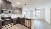 This well-appointed single-floor residence combines modern design with functional living spaces throughout. The open-concept kitchen is a standout, featuring dark espresso cabinetry, granite countertops, a subway tile backsplash, stainless steel appliances including a refrigerator, range, microwave, and dishwasher, and a peninsula that flows seamlessly into the living area. Light wood-style flooring runs through the main living spaces, enhancing the bright and airy atmosphere created by abundant natural light from multiple windows. The living area is equipped with a ceiling fan and offers direct access to a private balcony through a glass-panel door. Bedrooms are carpeted for comfort, each featuring ceiling fans and windows with exterior views. The primary bathroom impresses with a dual-sink granite vanity, dark-framed mirror, a glass-enclosed walk-in shower, and direct access to a spacious walk-in closet with built-in shelving. A second full bathroom mirrors the refined finishes, also offering a dual-sink granite vanity and glass shower enclosure. Crisp white walls, clean lines, and consistent use of dark matte hardware and fixtures throughout create a cohesive, contemporary aesthetic that is both stylish and inviting.