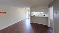 Located at 4341 Spring St in La Mesa, this single-floor unit offers a well-organized layout with a blend of practical finishes and comfortable living spaces. The main living area is generously sized, featuring rich wood-style flooring, a textured ceiling, and a ceiling fan that adds both airflow and a classic touch. Vertical blinds frame a sliding glass door that opens to an outdoor balcony, allowing natural light to fill the space and providing pleasant views of the surrounding greenery.

The kitchen is positioned adjacent to the living area and connected via a pass-through counter with open shelving above, creating an open and communicative feel between the two spaces. White cabinetry, a refrigerator, and an electric range complete the kitchen's functional setup, while a nearby window brings in additional natural light.

The bedroom is carpeted for comfort and features a large window with views of mature trees outside, offering a calm and private atmosphere. The bathroom is thoughtfully divided into two sections — a vanity area with a granite-style countertop, undermount sink, and framed mirror, which connects through to a separate water closet with wood-style flooring. The crisp white trim and neutral wall tones throughout the unit create a clean, cohesive aesthetic.
