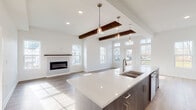 Located at 21 Forest Ridge Blvd in Mechanicville, NY, this thoughtfully designed single-floor home blends modern aesthetics with functional living. The heart of the home is an expansive open-concept kitchen and living area, where vaulted ceilings accented by rich dark wood beams create a dramatic yet welcoming atmosphere. The kitchen features a large center island with a white quartz countertop, stylish blue-gray cabinetry, stainless steel appliances, and pendant lighting that adds warmth to the space. The living area is anchored by a sleek linear fireplace and is bathed in natural light from multiple large windows and glass doors that lead to an outdoor deck. Light hardwood flooring flows throughout the main living areas, while plush carpeting adds comfort to the bedrooms. The primary bathroom offers a refined retreat with a dual-sink vanity, large-format tile flooring, and an elegantly tiled walk-in shower with brushed gold fixtures. A dedicated laundry room includes full-size GE washer and dryer units beneath a granite countertop with additional shelving. Entry corridors feature built-in coat hooks, and each room is finished with crisp white walls and clean trim, delivering a cohesive, contemporary feel throughout.