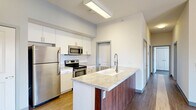 Located at 430 E Elm St in Springfield, MO, this thoughtfully designed two-bedroom, two-bathroom residence offers a clean, modern aesthetic across a well-utilized single floor. The open-concept living and dining area serves as the heart of the home, boasting hardwood-style flooring, soaring ceilings, and a striking pendant light fixture. A sliding glass door floods the space with natural light and opens to a private balcony with open views of the surrounding neighborhood and mature tree canopy. The kitchen is a standout feature, anchored by a granite-topped island with an undermount sink and rich wood-toned cabinetry. White upper cabinets and a full suite of stainless steel appliances — including a refrigerator, range, and microwave — complete the space with a polished, contemporary feel. Both bedrooms are carpeted and well-sized, with the primary offering generous proportions. The second bedroom features a large window with views of the tree-lined streetscape. Two full bathrooms provide functionality, each featuring light wood-tone flooring and a full soaking tub. Additional highlights include in-unit laundry, dedicated closet storage, a utility room, and a connecting hallway that keeps the layout organized and efficient.