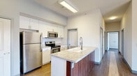 Located at 430 E Elm St in Springfield, MO, this thoughtfully designed two-bedroom, two-bathroom residence offers a clean, modern aesthetic across a well-utilized single floor. The open-concept living and dining area serves as the heart of the home, boasting hardwood-style flooring, soaring ceilings, and a striking pendant light fixture. A sliding glass door floods the space with natural light and opens to a private balcony with open views of the surrounding neighborhood and mature tree canopy. The kitchen is a standout feature, anchored by a granite-topped island with an undermount sink and rich wood-toned cabinetry. White upper cabinets and a full suite of stainless steel appliances — including a refrigerator, range, and microwave — complete the space with a polished, contemporary feel. Both bedrooms are carpeted and well-sized, with the primary offering generous proportions. The second bedroom features a large window with views of the tree-lined streetscape. Two full bathrooms provide functionality, each featuring light wood-tone flooring and a full soaking tub. Additional highlights include in-unit laundry, dedicated closet storage, a utility room, and a connecting hallway that keeps the layout organized and efficient.
