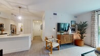 Located at 8209 Garden Catalina Circle in Lake Worth, Florida, this single-story residence presents a cohesive, contemporary design throughout its well-appointed layout. Light wood-look flooring flows continuously across the open floor plan, complementing the clean white walls and creating a bright, airy atmosphere.

The living area serves as the heart of the home, featuring large sliding glass doors that open directly onto a private patio, offering views of lush landscaping and the surrounding community. Natural light fills the space generously, enhancing its open and inviting character.

The kitchen is outfitted with white flat-panel cabinetry extending to the ceiling, stainless steel appliances, a subway tile backsplash, and a generous island with a white quartz countertop. Geometric pendant lighting adds a modern touch above the island.

A well-proportioned hallway connects the living areas to two bedrooms. The primary bedroom features warm yellow-toned walls, light flooring, and an en-suite bathroom with a walk-in glass shower, white vanity, and tasteful finishes. The second bedroom offers a ceiling fan, natural light from a window, and comfortable proportions. A second full bathroom includes a soaking tub with tiled surround and white cabinetry. Overall, the residence exudes a relaxed, modern Florida aesthetic.