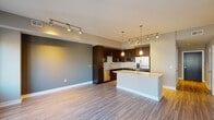 This contemporary single-floor residence showcases a thoughtfully designed open-concept layout that seamlessly connects the living and kitchen areas. The kitchen is a standout feature, equipped with stainless steel appliances including a French door refrigerator, electric range with microwave, and dishwasher. Dark espresso cabinetry extends from floor to ceiling, providing generous storage, while a textured tile backsplash adds visual interest. A large center island with a crisp white quartz countertop serves as both a workspace and casual gathering spot, illuminated by stylish pendant lighting. Track lighting runs throughout the main living area, which is finished with durable wood-style flooring that adds warmth to the neutral color palette.

The two bedrooms offer a quieter retreat, each carpeted in soft blue-grey and featuring windows that bring in natural light and views of the surrounding urban streetscape. Ceiling fans provide additional comfort. The bathroom is finished with large-format stone-look tile on both the floors and the tub surround, complemented by dark wood vanity cabinetry, granite countertops, and a generously sized mirror with contemporary vanity lighting. Overall, the space presents a clean, modern aesthetic with quality finishes throughout.