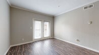 Located at 9955 Buffalo Speedway in Houston, TX, this well-appointed one-bedroom, one-bathroom residence offers a practical and comfortable single-floor layout. The open-concept living and kitchen area serves as the heart of the home, featuring rich hardwood-style flooring, crown molding, and neutral warm-gray walls that create a cohesive, modern aesthetic. French doors in the living area invite natural light and provide direct outdoor access. The kitchen is equipped with crisp white shaker cabinets, a subway tile backsplash, granite-style countertops, a breakfast bar peninsula, and a full suite of stainless steel appliances including a refrigerator, electric range, and microwave. Adjacent to the bathroom, a dedicated laundry area houses a full-size side-by-side washer and dryer with overhead wire shelving for additional storage. The bathroom features a single vanity with a speckled countertop and a tub-shower combination. The bedroom is carpeted for comfort, benefits from a ceiling fan, and includes a window with natural light and exterior views. A dedicated closet and hallway complete the layout, offering efficient use of the available space throughout.