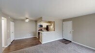 This single-floor residence offers a practical and comfortable layout designed for everyday living. The open-concept living area is finished with plush carpeting and neutral taupe walls, creating a warm, inviting atmosphere. A ceiling fan provides overhead lighting, while a sliding glass door fills the space with natural light and offers outdoor views.

The kitchen is positioned behind a peninsula-style breakfast bar with granite countertops, providing both a casual dining surface and a visual separation from the living area. Inside, the kitchen features white shaker-style cabinetry, matching granite countertops, stainless steel appliances including a refrigerator, microwave, and range, as well as wood-look flooring. An in-unit laundry area is accessible directly from the kitchen corridor.

The bedrooms are carpeted and finished in the same neutral tones, each offering closet storage. One bedroom features a window with a view to the outdoors, while the other includes direct access to a closet and hallway. The bathroom is equipped with a white vanity, granite countertop, a large mirror with bar lighting above, and a shower-tub combination, maintaining a clean, updated aesthetic throughout.