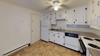 This single-floor, two-bedroom, one-bathroom unit offers a practical and straightforward layout. The kitchen is equipped with white cabinetry featuring black hardware, granite-style countertops, a stainless steel sink, and a full suite of white appliances including a refrigerator, electric range with overhead microwave, and dishwasher. Tile flooring and a ceiling fan add functionality to the space.

The living area is carpeted and open, flowing naturally toward the kitchen. A sliding glass door fills the room with natural light and provides direct access to a private balcony with outdoor views. A wall-mounted air conditioning unit and baseboard heating serve the space.

Both bedrooms are carpeted and feature baseboard heating, ceiling fans, and ample natural light from windows. One bedroom includes a built-in closet with louvered bifold doors, while the other offers a window with a roller shade.

The bathroom is clean and bright, featuring fully tiled walls surrounding a shower-tub combination, a window for natural light, and standard white fixtures including a toilet and vanity. Throughout the unit, crown molding and neutral tones create a cohesive, understated aesthetic.