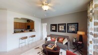 The Regent's 2-bedroom, 2-bathroom residence is a thoughtfully designed single-level home that balances comfort and functionality. The living room serves as the heart of the unit, featuring crown molding, a ceiling fan, and a sliding glass door that invites natural light and outdoor views. An arched passageway connects the living area to the kitchen, which is outfitted with warm honey-toned cabinetry, granite-style countertops, black appliances including a range, microwave, and refrigerator, and hardwood-style flooring. A breakfast bar provides a convenient casual dining option, while a separate dining area with crown molding offers a more formal setting. Both bedrooms are generously proportioned with plush carpet, ceiling fans, and large windows that fill each room with natural light. The primary bedroom features French doors opening to a private outdoor area. The primary bathroom includes a dual-sink vanity with ample cabinetry, a soaking tub, and natural light from a window. The second bathroom mirrors a similar clean aesthetic with a tub-shower combination and wood-look flooring. A dedicated in-unit laundry room with side-by-side washer and dryer adds everyday convenience to this well-appointed residence.