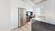 Located at 205 Avenue De l'Équinoxe in Brossard, this well-appointed 2-bedroom, 2-bathroom unit offers a thoughtfully designed layout across a single level. Light hardwood flooring flows throughout, complemented by striking exposed concrete ceilings that lend an industrial-modern character to the space. A welcoming hallway leads into the main living areas, where natural light filters in through generous windows. The kitchen is sleek and contemporary, featuring high-gloss white upper cabinetry, warm wood-toned lower cabinets, dark stone countertops, stainless steel appliances, and a central island — all anchored by exposed concrete overhead. Both bedrooms are well-proportioned and bright, with the primary bedroom benefiting from access to a dedicated walk-in closet fitted with wire shelving. The two bathrooms are finished with large-format floor tiles, glossy taupe wall tiles in the tub surround, and modern floating white vanities with integrated sinks. A spacious private balcony with glass railings extends the living space outdoors, offering open views of the surrounding Brossard cityscape. The unit's clean, minimalist aesthetic is consistent throughout, making it a refined and functional urban residence.