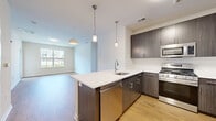 This thoughtfully designed 2-bedroom, 2-bathroom residence at 920 Belmont Ave in North Haledon, NJ offers a well-appointed single-floor layout with a clean, modern aesthetic. The open-concept kitchen and living area serves as the heart of the home, featuring a large center island with a crisp white quartz countertop, undermount sink, and stylish pendant lighting. Dark wood cabinetry provides rich contrast against the bright surroundings, while stainless steel appliances — including a gas range, microwave, dishwasher, and refrigerator — complete the contemporary kitchen. Warm hardwood flooring flows seamlessly throughout the entire residence, adding continuity and character to every room. The spacious living area is filled with natural light through generously sized windows and offers access to a private outdoor area. Both bedrooms are bright and well-proportioned, each featuring large windows with neighborhood views. The primary bedroom is notably spacious and includes a walk-in closet equipped with wire shelving and hanging rods for organized storage. The two bathrooms are finished with modern vanities featuring wood-toned cabinetry, large mirrors, white countertops, and tile flooring. One bathroom includes a glass-enclosed walk-in shower. A hallway connects the living spaces efficiently, contributing to the home's functional and comfortable flow.