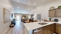 This well-appointed 2-bedroom, 2-bathroom single-floor home in Clarkston, Michigan offers a thoughtfully designed open-concept layout. The heart of the home is a seamlessly connected kitchen, dining, and living area bathed in recessed lighting beneath soaring vaulted ceilings. The kitchen is outfitted with rich warm-toned cabinetry, white quartz countertops, a double-basin sink, and a full suite of stainless steel appliances including a range, microwave, and refrigerator. A peninsula counter opens directly to the dining area, where light wood-look flooring extends throughout the main living spaces. The vaulted ceiling continues into the living room, enhancing the sense of openness. The generously sized primary bedroom features its own vaulted ceiling, plush carpet, large windows for natural light, and a ceiling fan. Its en-suite bathroom includes a dual-sink vanity with ample cabinetry and a walk-in glass-enclosed shower. The second bedroom is bright and versatile, with large windows and soft carpet. A dedicated laundry room houses a full-size Whirlpool washer and dryer with built-in shelving above. Two hallways connect the space efficiently, and a closet provides additional storage. This home balances comfort, function, and modern style throughout.