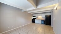 Located at 2701 NE Seventh St in Ocala, Florida, this two-story residence is efficiently laid out across two floors. The ground level houses an open-concept kitchen and living area finished with large-format light tile flooring and exposed structural beams on the ceiling, lending a clean, utilitarian aesthetic. The kitchen is equipped with white cabinetry, a single-basin sink, a black electric range with overhead ventilation, a black dishwasher, and a full-size black refrigerator — all arranged along a single wall for a streamlined look. An attached garage on the ground floor provides direct interior access and overhead door entry, offering practical storage or vehicle parking. A staircase connects the two levels, leading to the upper floor, which features carpeted bedrooms equipped with ceiling fans and ample natural light from windows. One upper-level room includes a distinctive arched window nook and open stairwell landing. A full bathroom on the upper level includes tile flooring, a tub-shower combination, toilet, and vanity with countertop. A dedicated laundry area houses a full-size washer and dryer beneath a sloped ceiling with wire shelving above. A closet provides additional storage. Neutral gray wall tones are carried throughout, creating a consistent and cohesive interior palette.