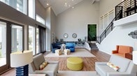 Located at 3920 Knickerbocker Pkwy in Raleigh, NC, this single-story community clubhouse offers a thoughtfully designed amenity space built for comfort and socializing. The centerpiece is a dramatic great room boasting soaring vaulted ceilings, hardwood-style flooring, and an abundance of natural light pouring in through oversized windows. The space is furnished with a mix of vibrant blue seating, colorful accent ottomans, and neutral sofas arranged across layered area rugs, creating distinct conversation zones. A built-in desk area lines the back wall beneath a pair of decorative round mirrors, providing a functional workspace. A modern chandelier and a sleek staircase with metal railings add architectural interest to the room.

Adjacent to the interior, a covered outdoor lounge features a full-height brick fireplace flanked by rattan chairs with bold orange cushions, offering a warm and inviting setting for year-round gatherings. French doors connect this area directly to the expansive resort-style pool deck, which is lined with lounge chairs, shaded by orange umbrellas, and anchored by a charming poolside gazebo surrounded by mature trees.

Rounding out the amenities is a dedicated billiards room, complete with a full-size pool table, vibrant abstract artwork, high-top tables, and a wet bar with white cabinetry — an ideal setting for leisure and entertainment.