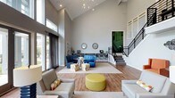 Located at 3920 Knickerbocker Pkwy in Raleigh, NC, this single-story community clubhouse offers a thoughtfully designed amenity space built for comfort and socializing. The centerpiece is a dramatic great room boasting soaring vaulted ceilings, hardwood-style flooring, and an abundance of natural light pouring in through oversized windows. The space is furnished with a mix of vibrant blue seating, colorful accent ottomans, and neutral sofas arranged across layered area rugs, creating distinct conversation zones. A built-in desk area lines the back wall beneath a pair of decorative round mirrors, providing a functional workspace. A modern chandelier and a sleek staircase with metal railings add architectural interest to the room.

Adjacent to the interior, a covered outdoor lounge features a full-height brick fireplace flanked by rattan chairs with bold orange cushions, offering a warm and inviting setting for year-round gatherings. French doors connect this area directly to the expansive resort-style pool deck, which is lined with lounge chairs, shaded by orange umbrellas, and anchored by a charming poolside gazebo surrounded by mature trees.

Rounding out the amenities is a dedicated billiards room, complete with a full-size pool table, vibrant abstract artwork, high-top tables, and a wet bar with white cabinetry — an ideal setting for leisure and entertainment.