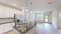 Located at 40 Pallet Rd in Candler, NC, this single-story, 2-bedroom, 2-bathroom home offers a thoughtfully designed open-concept layout with modern finishes throughout. The kitchen serves as the heart of the home, featuring white shaker cabinetry, dark granite countertops, a tile backsplash, stainless steel appliances including a French door refrigerator, electric range, and microwave, and a central island with pendant lighting and an undermount sink. Light hardwood-style flooring flows seamlessly from the kitchen into the living area, which is brightened by large windows and a ceiling fan. The primary bedroom is generously sized with plush carpeting, a ceiling fan, and direct access to its en-suite bathroom. The primary bath showcases a double-sink vanity with granite countertops, white cabinetry, and wood-style flooring, with a walk-in closet offering wire shelving for ample storage. The second bedroom also features carpeting, a ceiling fan, and natural light. A dedicated laundry room houses a Whirlpool front-load washer with overhead wire shelving. The home also includes a patio, two closets, and a clean, neutral color palette throughout, creating a bright and inviting atmosphere.