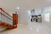 Located at 36 Third St, Unit 105, in Fall River, MA, this two-floor unit offers a thoughtfully designed layout spread across two distinct levels. The main floor impresses immediately with its soaring double-height ceilings, creating a dramatic sense of vertical space. Polished tile flooring reflects natural light admitted through multiple windows fitted with roller shades, while pendant lighting adds a modern touch overhead. A sleek recessed-lit lower area provides additional functional space beneath the upper level overhang. The staircase is a standout architectural feature — crafted from rich warm-toned wood with dark metal balusters and sturdy newel posts, it connects both floors with style and character. A wood-paneled entry door grounds the lower level with a welcoming, solid presence. The upper floor offers an open, light-filled space with smooth luxury vinyl flooring, recessed ceiling lights, and a large window that frames views of the surrounding neighborhood. A wood-and-iron railing lines the open mezzanine edge, maintaining visual connectivity with the floor below. The bathroom is finished to a high standard, featuring large-format tile flooring, a dark wood vanity with granite countertop, a backlit mirror, and a walk-in shower with white subway tile surround.