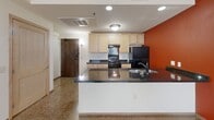 This single-floor unit on Fourth Street East in Saint Paul, Minnesota, presents a well-organized layout with consistent design elements throughout. The kitchen serves as a central highlight, featuring light maple cabinetry paired with dark granite countertops, a black appliance suite including a gas range and refrigerator, and a double-basin sink. A bold terra cotta accent wall adds a distinctive visual element, complementing the neutral tones found elsewhere in the space. The kitchen also includes a peninsula that provides additional prep space and a natural division between the cooking area and the adjoining room. Terrazzo flooring is a unifying feature found consistently throughout the unit, offering a durable and visually textured surface. The bathroom includes a maple vanity with dark granite countertops, a single undermount sink, and a large mirror, with terrazzo flooring continuing from the adjacent rooms. The bedroom offers ample space with two closets fitted with hanging rods, light maple doors, and clean white walls that maximize brightness. Windows with wood-framed casings allow natural light to enter multiple rooms. Recessed and flush-mount lighting provides consistent illumination throughout. The overall ambiance is practical and cohesive, with warm wood tones and bold accent colors creating a balanced interior character.