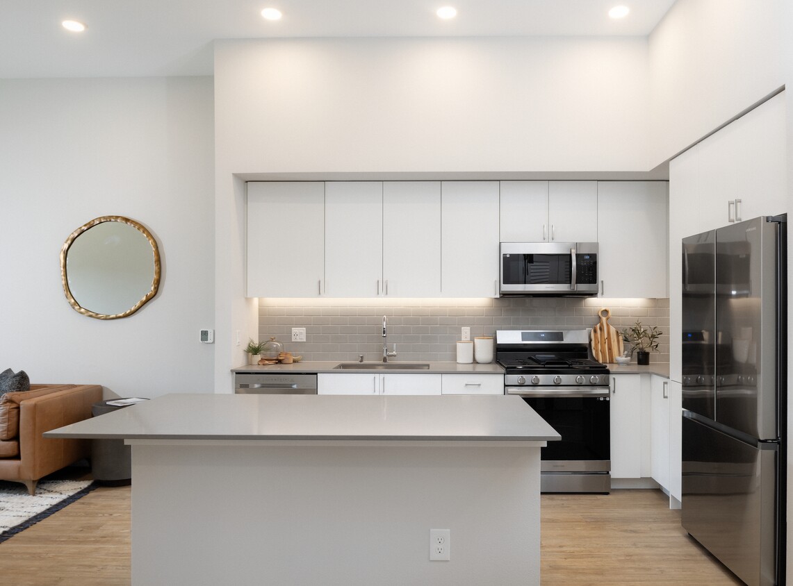 Kitchen with grey quartz countertops, white cabinetry, grey subway tile backsplash, stainless steel appliances, and hard surface flooring - Avalon Bothell Commons