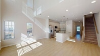 Located at 4700 Prosperity Church Road in Charlotte, NC, this two-story home offers a thoughtfully designed layout across two floors. The main level opens with a dramatic two-story living area, where soaring ceilings and large windows with plantation-style blinds flood the space with abundant natural light, highlighting the clean lines of the light hardwood flooring throughout. The open-concept layout seamlessly connects the living room, dining area, and kitchen, making it ideal for everyday living and entertaining. The kitchen is a standout, featuring crisp white cabinetry, granite countertops, stainless steel appliances including a French door refrigerator and built-in microwave, and a central island with pendant lighting overhead. A pantry and utility spaces add to the practicality of the main floor. Upstairs, three bedrooms provide comfortable retreats, each carpeted and equipped with closets — including a spacious walk-in closet with wire shelving in the primary suite. The secondary bedrooms feature ceiling fans and double-door closets. Three full bathrooms serve the home, including one with a tub-shower combination and granite vanity. Outside, a concrete walkway leads to dedicated parking, with open surroundings and mature trees framing the property.