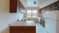 This single-floor residence at 777 W State Street in Trenton, NJ offers a well-organized layout comprising one bedroom, one and a half bathrooms, and a versatile den. Rich parquet wood flooring extends throughout the living areas and bedroom, lending warmth and classic character to the space.

The kitchen is a functional highlight, featuring rich dark wood cabinetry with decorative detailing, a central island that provides additional prep and storage space, a four-burner electric range, dishwasher, and refrigerator. Light tile flooring and a window with natural light complete the kitchen's practical design.

The spacious living area is open and airy, with gleaming parquet floors and multiple windows that bring in natural light, creating a bright and welcoming atmosphere. The bedroom is generously sized, also finished with parquet flooring, and offers access to an adjacent hallway with closet storage.

The full bathroom is clean and well-maintained, featuring a tiled shower and tub combination with classic white square tile surround and chrome fixtures. A half bathroom provides added convenience for guests.

The den adds flexibility to the floor plan, suitable for use as a home office, reading room, or additional living space. Overall, the residence presents a tidy, functional layout with consistent finishes and a comfortable, livable ambiance throughout.