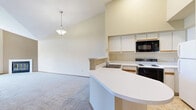 Located at 9900 Briar Rd in Bloomington, MN, this one-bedroom, one-bathroom unit offers a thoughtfully designed single-floor layout. The living room is the standout centerpiece, boasting dramatic vaulted ceilings that soar to impressive heights, a white-surround fireplace, and an arched transom window paired with a large picture window that frames lush outdoor greenery and a private balcony beyond. Plush carpet runs throughout the main living areas, enhancing the warm, comfortable atmosphere. The open-concept kitchen, dining, and living area flows seamlessly together. The kitchen features a curved peninsula countertop, white cabinetry, built-in appliances including a microwave and range, and a double sink — all beneath a skylight that adds brightness to the space. A hallway entry with tile flooring leads into the unit, with warm wood-toned doors and trim providing classic detailing throughout. The spacious bedroom includes a dedicated closet with built-in shelving and a window overlooking the outdoors. The full bathroom is cleanly appointed with a tub/shower combination, vanity, and tile flooring. This well-proportioned unit offers a generous sense of space and a welcoming ambiance suited for comfortable everyday living.