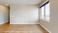 This well-designed 2-bedroom, 2-bathroom residence offers a thoughtfully laid-out single floor with a clean, contemporary aesthetic throughout. The open-concept kitchen and living area serves as the heart of the home, featuring warm wood-toned cabinetry in two complementary finishes, stainless steel appliances including a refrigerator, range, and built-in microwave, and a white quartz peninsula countertop illuminated by stylish pendant lighting. Light wood-look flooring runs consistently throughout the main living areas and bedrooms, adding warmth and visual continuity. The primary bedroom is a generously sized retreat with multiple large windows that frame sweeping city views, filling the room with natural light. The second bedroom also offers ample space, natural light, and a double-door closet. Both bathrooms are finished with neutral tile flooring, wood-grain vanity cabinetry, white quartz countertops, and framed mirrors. One bathroom features a glass-enclosed walk-in shower with white subway tile, while the second includes a similarly refined vanity setup. Connecting hallways and transitional spaces are clean and well-proportioned, reinforcing the residence's efficient and functional design. Neutral warm-gray wall tones throughout create a calm, cohesive atmosphere suited to a variety of interior styles.