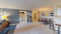 This single-floor residence offers a thoughtfully designed layout that balances comfort and functionality across several well-defined living spaces. The open living room is bright and inviting, featuring crown molding, plush carpeting, a bold slate-blue accent wall, and large windows that allow generous natural light to fill the room. An adjoining dining area accommodates a full dining set beneath a stylish pendant light fixture, creating an ideal space for everyday meals or entertaining. The kitchen is equipped with white cabinetry, ample counter space, a stainless steel range, built-in microwave, dishwasher, and a full-size refrigerator, all set atop tile flooring. A dedicated in-unit laundry closet with side-by-side washer and dryer adds everyday convenience. The primary bedroom is generously sized with a teal accent wall, carpeted flooring, a large window with outdoor views, and direct access to an en-suite bathroom. A second bedroom mirrors this comfortable aesthetic with its own accent wall and ample natural light. Both bathrooms feature soaking tub and shower combos with tile surrounds, neutral wall tones, and framed wall art, offering a clean and polished finish throughout.