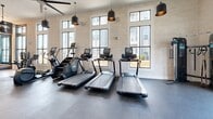 This 690-square-foot fitness center showcases a thoughtfully designed layout optimized for exercise and wellness. The space boasts high ceilings and an abundance of natural light streaming through large windows, creating an open and inviting atmosphere. Sleek white brick walls contrast beautifully with the dark flooring, while modern pendant lights and ceiling fans provide both illumination and air circulation.

The gym is equipped with a comprehensive range of fitness apparatus, including multiple treadmills, elliptical machines, stationary bikes, and weight training equipment. A separate area is dedicated to free weights and exercise balls, catering to diverse workout preferences. The arrangement of equipment allows for efficient use of space while maintaining ample room for movement.

Stylish design elements, such as the "SOAR" signage and carefully placed decor, add character to the functional space. The center also features convenient amenities like water stations and storage solutions. With its blend of practicality and aesthetic appeal, this fitness center offers an ideal environment for health and exercise enthusiasts.