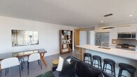 This single-floor residence at Morgan Parc, located at 199 2nd Street in Mineola, NY, showcases a thoughtfully designed open-concept layout that seamlessly connects the living, dining, and kitchen areas. Large windows flood the space with natural light while offering views of the surrounding neighborhood.

The kitchen is a standout feature, equipped with stainless steel appliances including a gas range, built-in microwave, and French door refrigerator. White cabinetry extends to the ceiling, complemented by a subway tile backsplash and a generous waterfall-edge island with quartz countertops and bar seating. Sleek pendant lighting adds a modern touch overhead.

The living and dining area is expansive, highlighted by a striking large-scale abstract wall mural that serves as a bold focal point. Large-format tile flooring runs throughout the common areas, contributing to the clean, contemporary aesthetic.

The bedroom is generously sized with floor-to-ceiling windows that invite natural light and provide open exterior views. Dark hardwood flooring adds warmth and contrast to the neutral walls.

The bathroom features marble-look tile in a herringbone pattern, a backlit vanity mirror, wood-accented cabinetry, and refined finishes throughout. A dedicated in-unit laundry closet with a stacked washer and dryer adds everyday convenience.