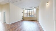 This well-appointed 3-bedroom, 2-bathroom unit offers a compelling blend of urban industrial character and modern comfort across a single floor. Warm hardwood flooring runs throughout the living areas and bedrooms, lending a cohesive and inviting feel to the entire space. The open living area is highlighted by exposed structural columns, track lighting along the ceiling, and large multi-pane windows that flood the room with natural light and frame views of the surrounding cityscape. The bedrooms are generously proportioned, with elevated ceilings accented by exposed beams and ample closet space featuring built-in shelving. The kitchen is thoughtfully designed with dark cabinetry, stone-look countertops, a classic subway tile backsplash, and a full suite of stainless steel appliances including a refrigerator, electric range, and dishwasher. An in-unit washer is also conveniently located within the kitchen area. The two bathrooms offer clean, functional designs — one featuring a soaking tub and the other a walk-in shower with tiled surrounds. Overall, the space delivers an airy, loft-inspired ambiance with practical amenities suited for urban living.