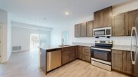 This well-appointed single-floor residence offers a thoughtfully designed layout that balances functionality and modern style throughout. The open-concept kitchen serves as the heart of the home, featuring rich dark-stained cabinetry extending to the ceiling for ample storage, granite-look countertops, and a full suite of stainless steel appliances including a refrigerator, electric range, over-the-range microwave, and dishwasher. A peninsula with an undermount sink provides additional prep space and a natural divide between the kitchen and the bright living area, which is finished with light wood-look flooring and a sliding glass door that invites natural light and opens to an outdoor space. The bedrooms offer a calm, neutral atmosphere with plush carpeting and windows that bring in outdoor views. A full bathroom includes a granite-topped vanity with an undermount sink, a tub-shower combination, and clean tile flooring. A generously sized walk-in closet features multi-tier wire shelving systems, providing exceptional storage capacity. The dedicated in-unit laundry room accommodates a full-size washer and dryer and includes additional overhead shelving. Light wood-look flooring flows through the main living areas, tying the space together with a cohesive, contemporary aesthetic.