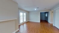 This single-floor space offers a practical and well-designed layout with consistent warm-toned hardwood flooring throughout the main living areas. The entry foyer welcomes you with a tiled threshold and a solid front door flanked by a narrow window that allows natural light to filter in.

The main living area is generously proportioned, featuring a fireplace with a clean white mantel, neutral gray walls, and French doors that open to the outdoors, filling the room with natural light. Ceiling-mounted light fixtures and HVAC vents are strategically placed throughout for comfort.

The kitchen is efficiently laid out with warm-toned cabinetry featuring frosted glass inserts, granite countertops, a white subway tile backsplash, and a full suite of stainless steel appliances including a refrigerator, dishwasher, range, and microwave. Light tile flooring completes the kitchen's functional aesthetic.

Additional rooms offer flexible use, with neutral walls, hardwood flooring, and ample wall outlets. The bathroom features a wide vanity with granite countertops, white cabinetry, a large mirror, and elegant overhead lighting, creating a clean and functional space throughout.