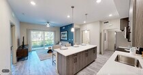 Located in Naples, FL, this well-appointed 2-bedroom, 2-bathroom single-floor residence offers a thoughtfully designed open-concept layout with modern finishes throughout. Light wood-tone flooring runs seamlessly across the living areas, complementing the neutral color palette accented by a bold teal feature wall in the living room.

The kitchen is a standout, featuring wood-grain cabinetry extending to the ceiling, stainless steel appliances, a white quartz countertop, a subway tile backsplash, and a central island with pendant lighting and bar seating — ideal for casual dining or entertaining. The living room is bright and welcoming, with a ceiling fan and sliding glass doors that open to lush outdoor greenery, bringing in natural light and Florida's scenic surroundings.

The primary bedroom is generously proportioned, offering a ceiling fan, a closet, and direct sightlines to the kitchen. The second bedroom is equally serene. Both bathrooms are finished with wood-tone vanities, white quartz countertops, and light tile flooring. One bathroom features a glass-enclosed walk-in shower, while the other includes a full soaking tub. A dedicated laundry closet houses a full-size Whirlpool washer and dryer, completing this well-equipped home.
